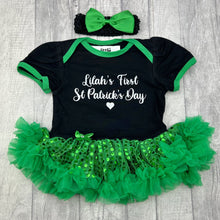 Load image into Gallery viewer, Baby girls short sleeve black with green sequin tutu romper and matching bow headband above. The tutu romper features white glitter script lettering saying Name's First St Patrick's Day.
