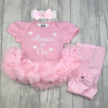 Load image into Gallery viewer, Baby girls light pink tutu romper with bow headband above and pink tights on the right side. The tutu romper features white glitter love hearts design and script lettering saying Name is One.