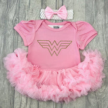 Load image into Gallery viewer, Baby girls short sleeve light pink tutu romper with bow headband above. The tutu romper features a gold glitter wonder woman logo.
