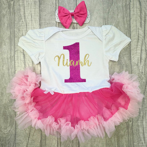 Baby girls white with pink tutu romper and matching bow headband above. The tutu romper features pink number 1 and personalised name in gold over the top