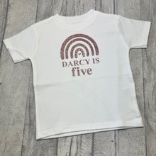 Load image into Gallery viewer, White t-shirt with 'Darcy is five' text and rainbow design on a wooden surface
