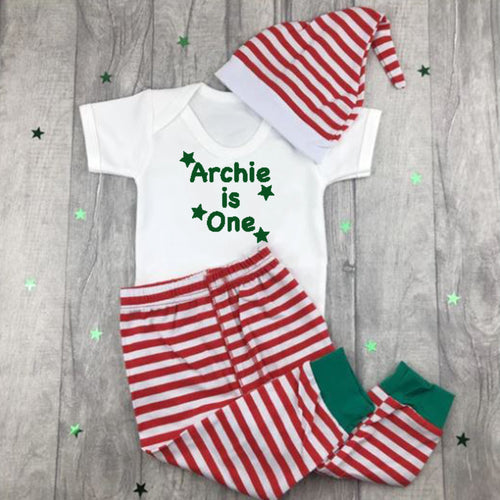 White short sleeve romper with green star design and text on. Red and white striped pants and hat.