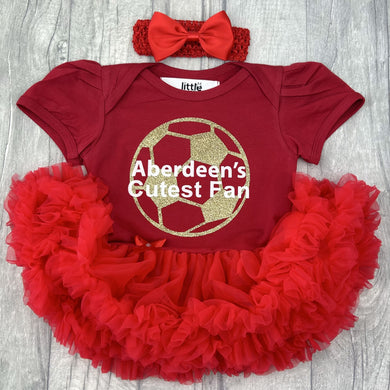 Baby girls red short sleeve tutu romper with bow headband above. The tutu romper features gold glitter football design and white text central over the top saying Aberdeen's Cutest Fan.