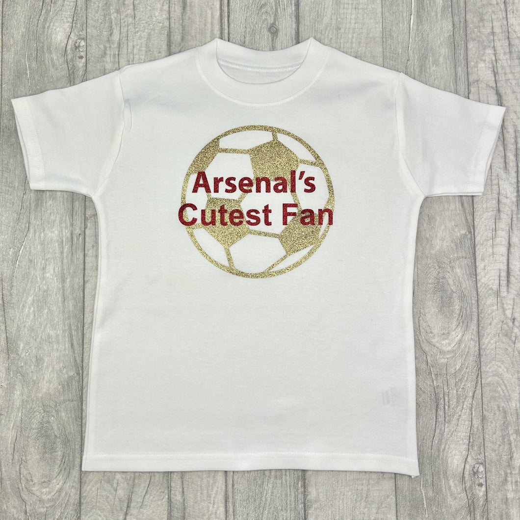 White T-shirt featuring gold football design with red text over the top saying Arsenal's Cutest Fan