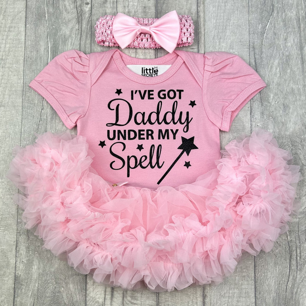 Baby girls light pink tutu romper with matching bow headband above. The tutu romper features black glitter stars and wand design with lettering saying I've got Daddy under my spell.