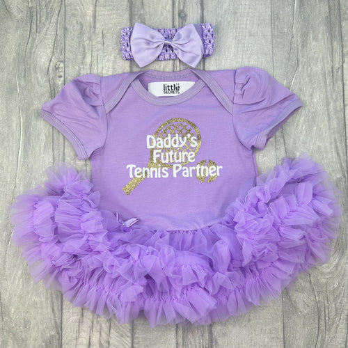 Baby girls light purple tutu romper with bow headband above. The tutu romper features a gold glitter racket and ball design with white lettering over the top saying Daddy's Future Tennis Partner