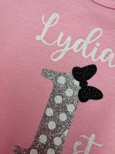 Load image into Gallery viewer, Close-up of a pink garment with glittery silver cursive text reading 'Lydia' and a glittery silver number 1 decorated with white polka dots and a black bow.

