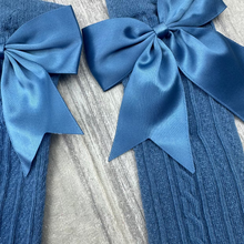 Load image into Gallery viewer, Two blue ribbed knit leg warmers with large matching satin bows, displayed on a gray wood-textured surface.
