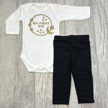 Load image into Gallery viewer, Long sleeve white romper and black leggings. The romper features gold glitter moon and stars circle design with lettering in the middle saying My First Eid.
