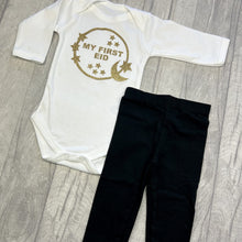 Load image into Gallery viewer, Long sleeve white romper and black leggings. The romper features gold glitter moon and stars circle design with lettering in the middle saying My First Eid.
