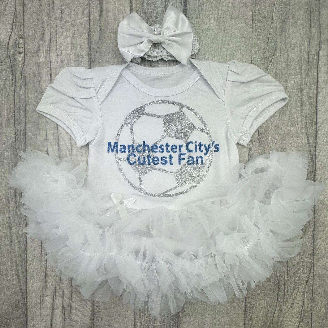 Baby outfit with 'Manchester City's Cutest Fan' text on a white shirt with ruffled skirt and headband.