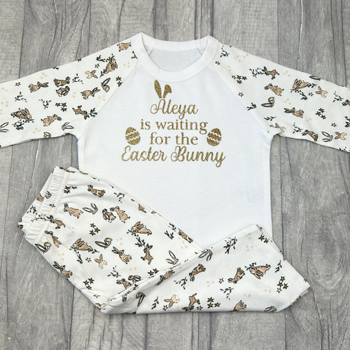 Long sleeve bunny print pyjama set. The top features gold glitter bunny ears and easter egg design with lettering saying Personalised Name is waiting for the Easter Bunny.