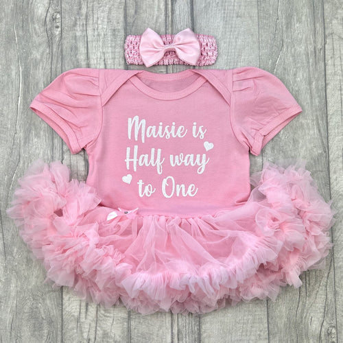 Baby girls light pink short sleeve tutu romper with matching bow headband above. The tutu romper features white glitter love heart design with script text saying 'is Half way to One'