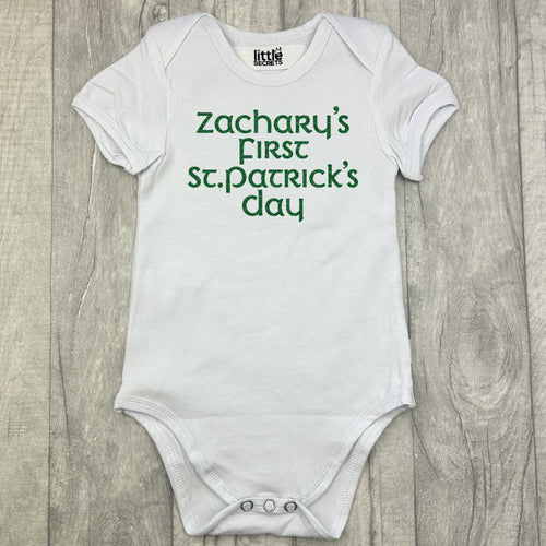 Babies white romper bodysuit, featuring green glitter lettering saying Personalised name's First St Patrick's Day