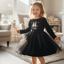 Load image into Gallery viewer, A young girl stands barefoot in a bright living room wearing a black long-sleeve dress with a tulle skirt and a white graphic on the chest.
