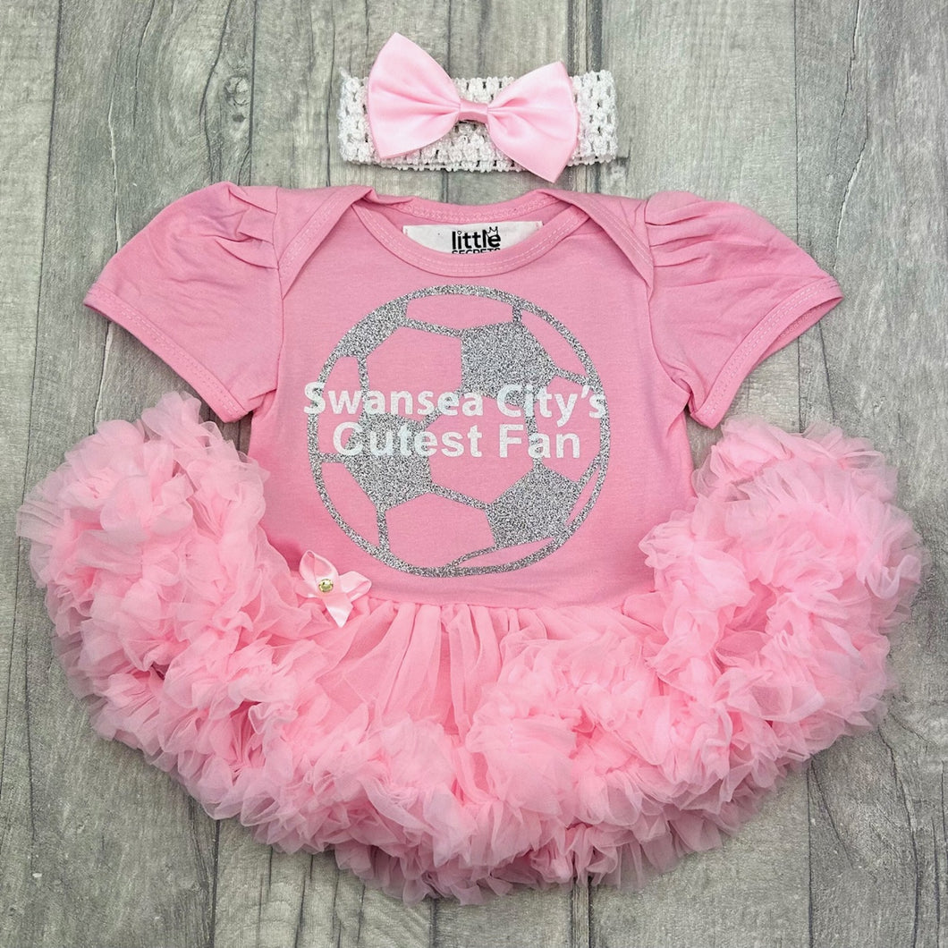 Baby girls short sleeve pink tutu romper with bow headband above. The tutu romper features a silver football design with white lettering over the top saying Swansea City's Cutest Fan.