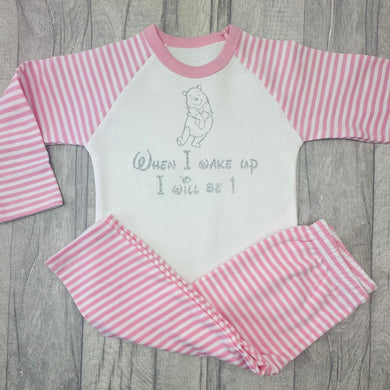 Pink and White striped girls pyjama set. The top features a silver glitter Winnie the Pooh design with lettering underneath saying When I wake up I will be 1.
