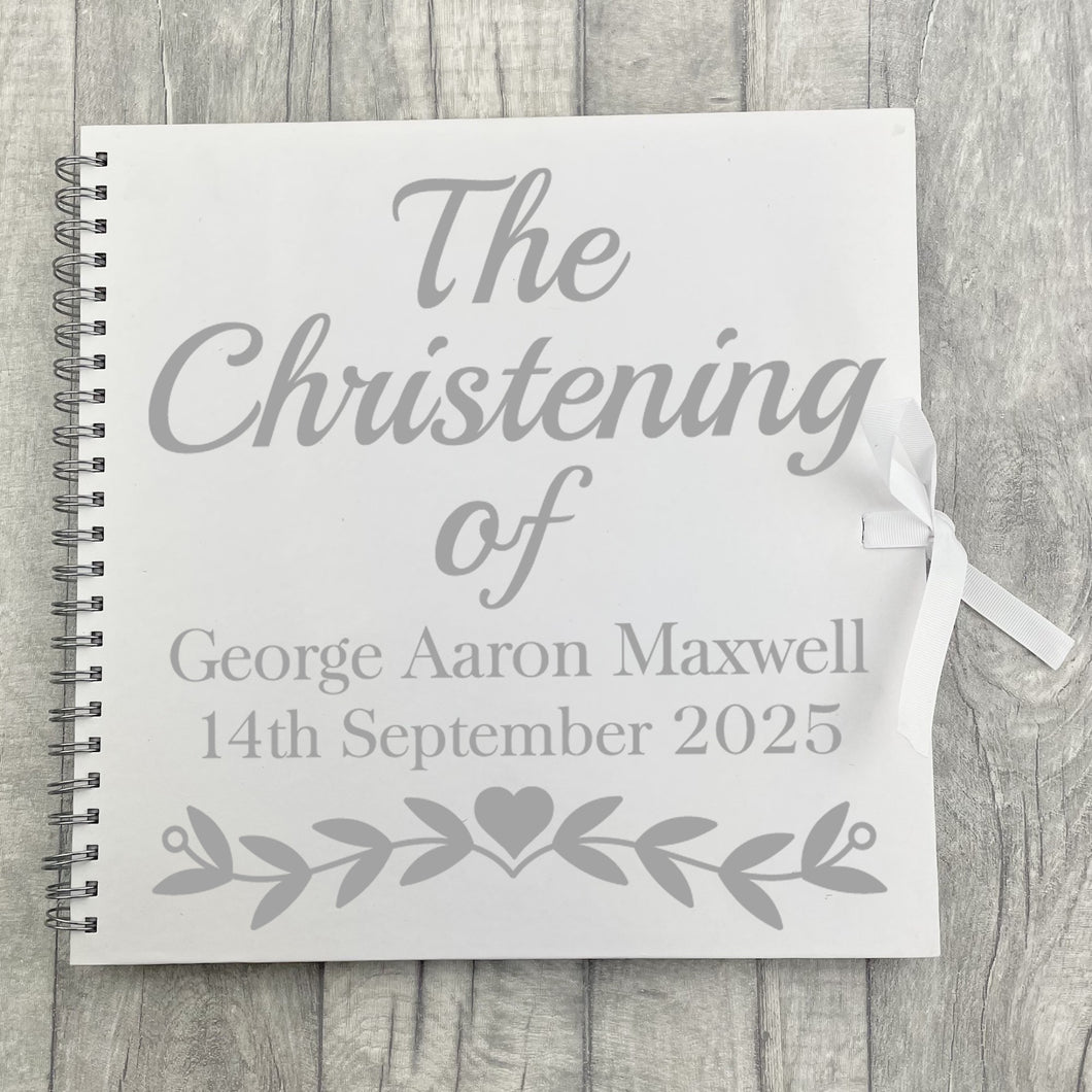 Spiral bind white large scrapbook with white ribbon tie fasten. The cover of the scrapbook features silver lettering saying The Christening of Personalised Name and Date.