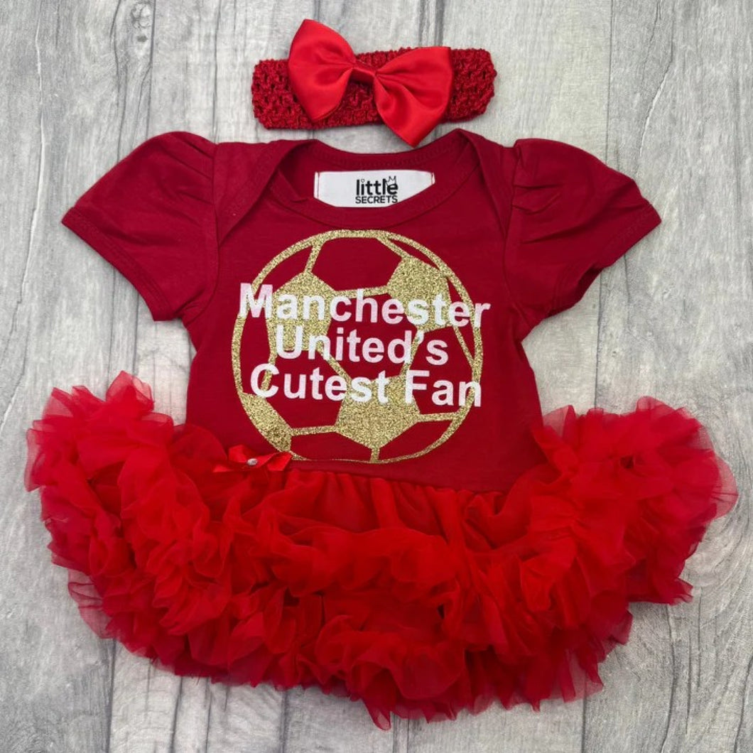 Baby girls short sleeve red tutu romper with bow headband above. The tutu romper features a gold glitter football design with white lettering central over the top saying Manchester United's Cutest Fan.